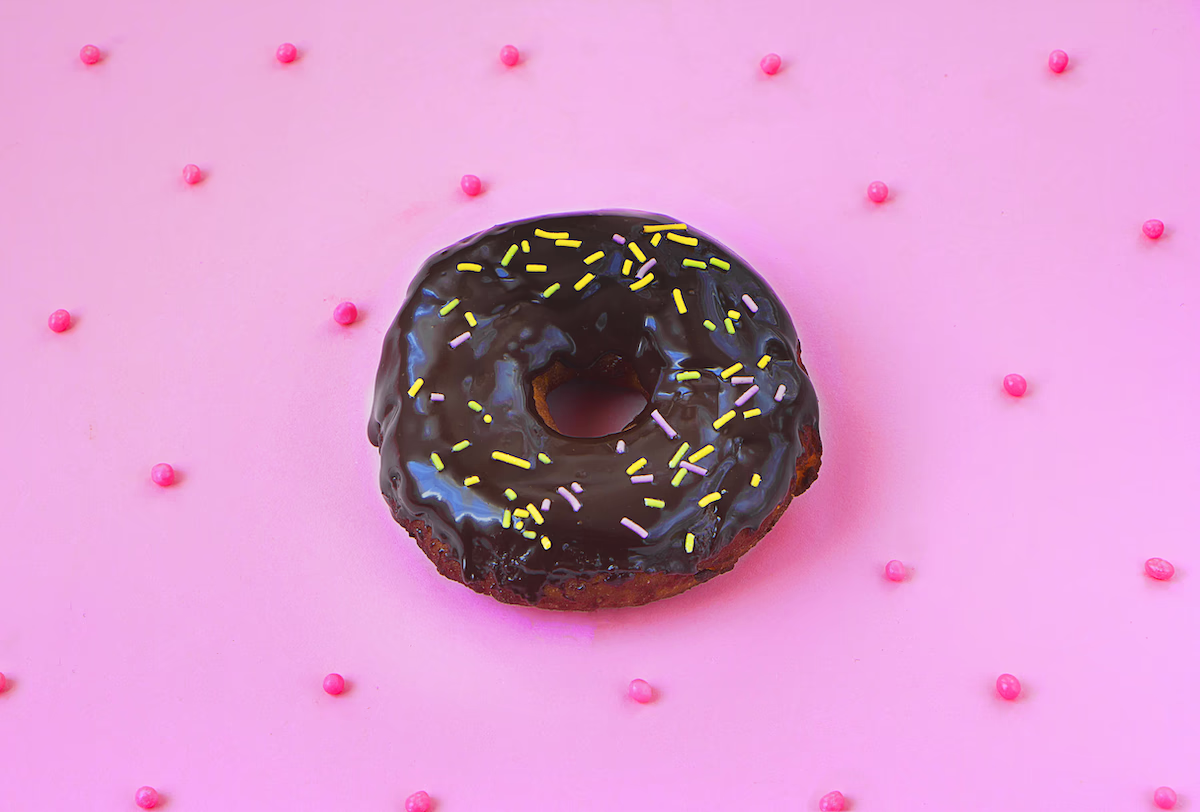 Chocolate donut with sprinkles on pink background with pink dots.